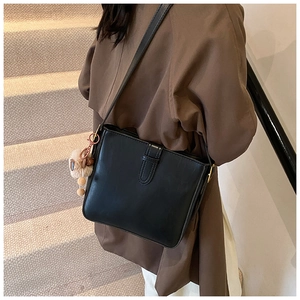 Sac seau chic en cuir noir mat avec breloque en peluche porté à l'épaule pour femme