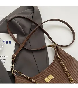 Detail of brown pleated leather shoulder bag with gold chain on grey blazer