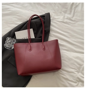 Detail view of large dark red leather tote bag styled with a black blazer and art book