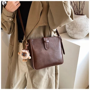 Détail d'un sac bandoulière en cuir marron foncé avec pendentif lion en peluche et fermoir métal