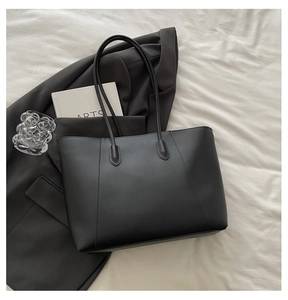 Detail of a black leather tote bag on white fabric with a blazer and arts book