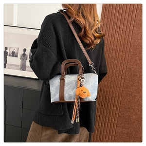 Detail of light blue denim pillow bag with orange puppy charm and leather trim