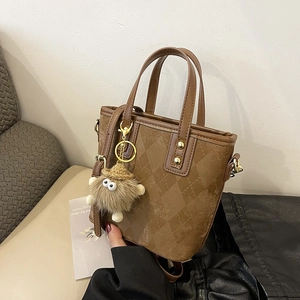 Dettaglio di una borsa a secchiello marrone trapuntata con un simpatico charm mostro