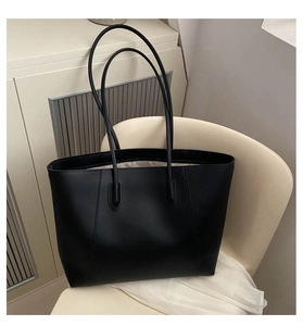 Detail of minimalist black tote bag with long straps on a modern chair in a studio