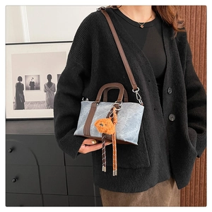 Detail of grey-blue textured mini tote with orange bear charm and brown leather straps