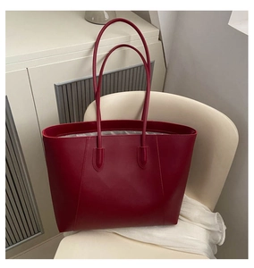 Detail of burgundy leather tote bag with long shoulder strap on minimalist beige chair