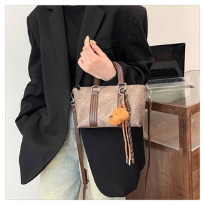 Close-up of retro texture handbag featuring a plush bear charm and elegant leather handles