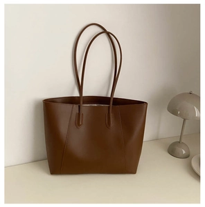 Detail of a brown large capacity tote bag with minimalist V-stitch and slender handles