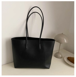 Minimalist black faux leather tote bag displayed with a modern lamp and pastries