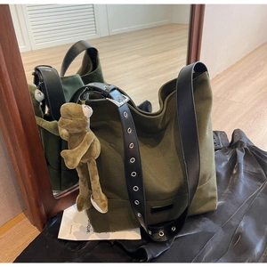 Olive green canvas tote bag with metal eyelet strap and plush frog charm accessory