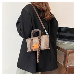 Retro brown canvas bucket bag with plush puppy pendant shown on person's shoulder