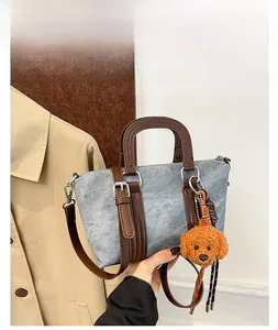 Detail view of light blue denim bucket bag with brown leather strap and teddy charm