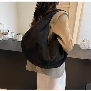Détail d'un grand sac fourre-tout noir mat porté par un mannequin dans un café minimaliste