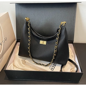 Detail view of black pleated leather handbag with gold chain in a premium gift box