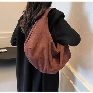 Close-up of a rust red suede hobo tote bag worn over a black winter coat