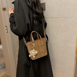 Borsa a secchiello marrone con motivo a rombi e ciondolo a mostriciattolo su cappotto nero