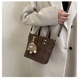 Dettaglio borsa a secchiello trapuntata marrone scuro con ciondolo di peluche su modella