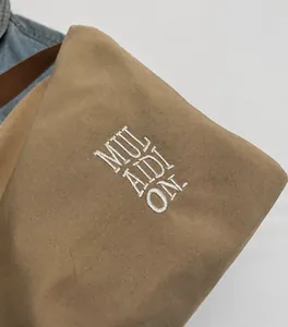 Vista de detalle de bolso tote en lona caqui con bordado blanco y correa de cuero de calidad