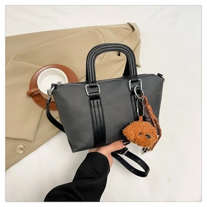 Detail view of a black Boston handbag featuring a cute teddy bear charm and strap