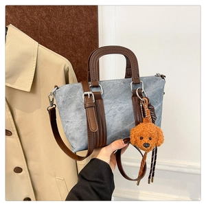 Detail of blue denim pillow bag featuring brown leather straps and a cute teddy charm