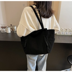 Detail der schwarzen Cord-Einkaufstasche mit Rippstruktur und Seitentasche im Café-Ambiente