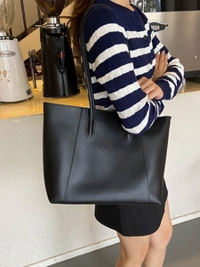 Minimalist black leather tote bag with long straps for commute shown in a cafe setting