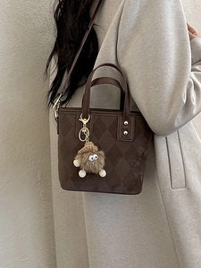 Borsa a secchiello marrone a scacchi con manici in pelle e ciondolo peluche indossata