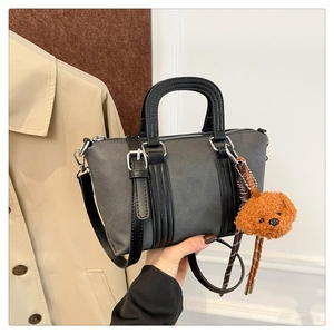 Detail of dark grey pillow bag with black leather handle and brown teddy bear charm