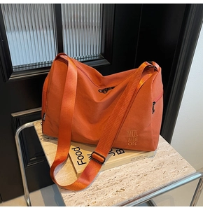 Detalle del bolso tote de lona naranja con bordado sobre fondo de mármol elegante