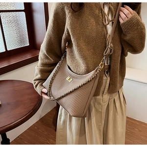 Detail of beige pleated bucket bag with gold chain and turn-lock closure on shoulder