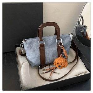 Detail of light blue denim crossbody bag with brown straps and a cute plush puppy pendant