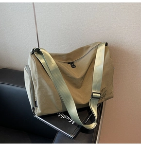 Detalle de bolso bandolera de nailon caqui con correa ancha sobre un asiento de cuero