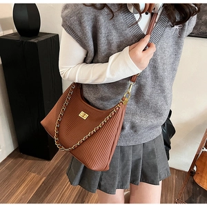 Detail of a brown pleated crossbody bag featuring a gold twist lock and metal chain strap