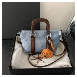 Detailed view of light blue denim tote bag with brown leather handles and plush dog charm
