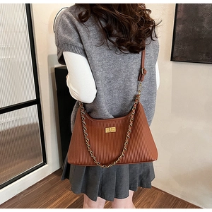 Detail view of retro brown pleated tote bag with golden chain strap on a model's shoulder