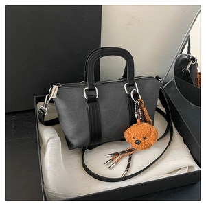 Close-up of grey leather satchel with teddy bear charm in a luxury display box