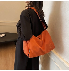 Detalle de un bolso tote grande naranja brillante con bordado MULAIDI en modelo femenino