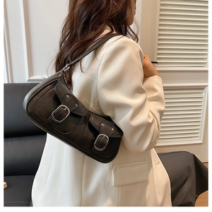 Detail of black matte leather shoulder bag with double buckle straps on white blazer