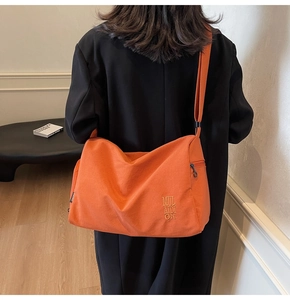 Detalle de bolso bandolera de lona naranja vibrante con logo bordado y correa ancha