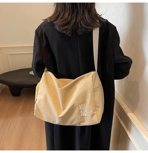 Detalle de bolso hobo de lona beige con bordado MUL AIDI ON y correa ancha al hombro