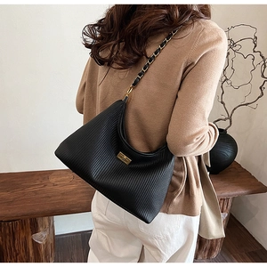 Detailed close-up of pleated black leather shoulder bag with gold chain strap and turn-lock