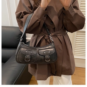 Chic black faux leather shoulder bag with vintage dual pockets worn over a brown trench coat