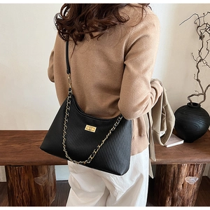 Detail of black pleated shoulder bag featuring a gold clasp and elegant chain strap