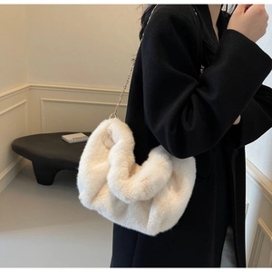 Close-up of fluffy faux fur cloud bag with thin gold chain strap on black coat