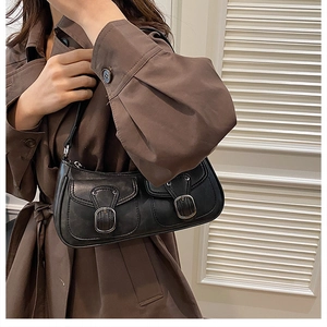 Detailed view of a retro black leather underarm bag with metal buckles on a model