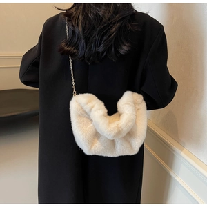 Detail of soft cream faux fur crossbody bag with elegant gold chain strap on black coat