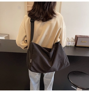 Detalle del bolso bandolera negro de gran capacidad con bordado y correa ancha