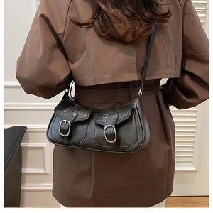 Detail of vintage black faux leather shoulder bag with silver buckle flap pockets on a model