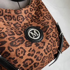 Detail der Leopard-Tasche mit silbernem M-Logo aus Metall und schwarzem Lederriemen