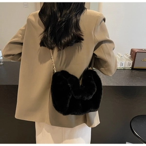 Chic black faux fur heart-shaped crossbody bag with gold chain strap worn over an outfit